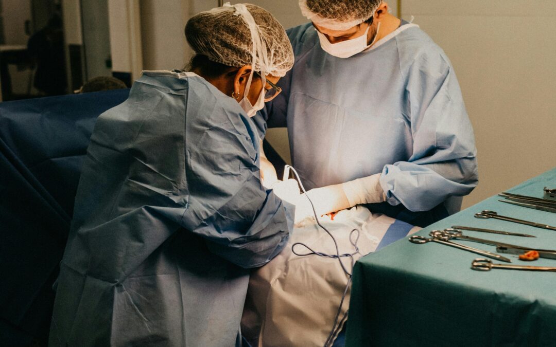 Medical Professionals Performing An Autopsy In A Sterile Environment, Wearing Surgical Gowns, Masks, And Gloves, With Surgical Instruments Arranged On A Table Nearby.